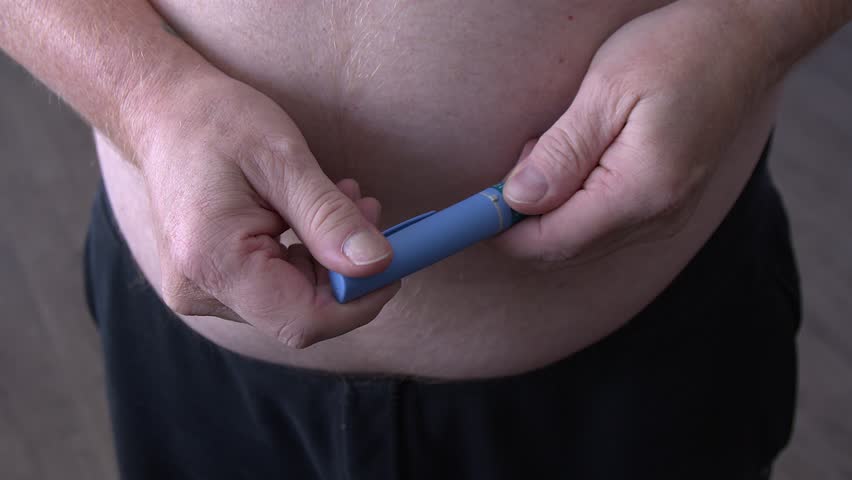 Fat man prepares to add needle to medication injector pen, large belly