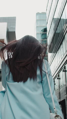 stylish asian woman in blue trench walking city street turning back smiling vertical video elegant fashion confident modern lifestyle urban chic feminine confidence minimal style trend