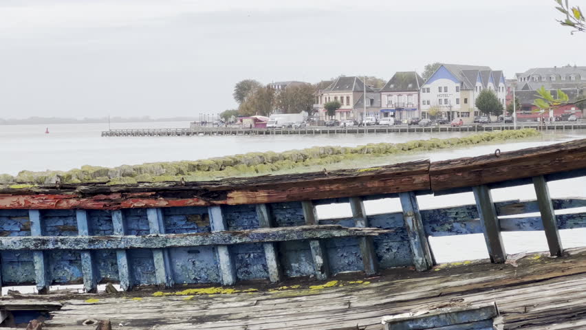 Close-up view of an old abandoned wooden fishing boat wreck with peeling blue and red paint, weathered planks and decaying structure lying on the shore of the Baie de Somme in Le Crotoy, France
