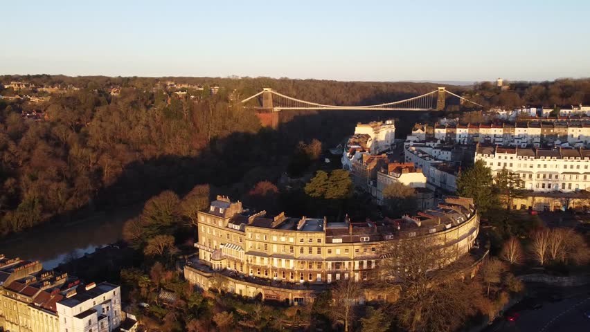 Aerial view of Clifton, Bristol, UK. Scenic drone footage capturing the Georgian architecture of Clifton, the iconic Clifton Suspension Bridge and surrounding woodland at golden hour. Cityscape view.