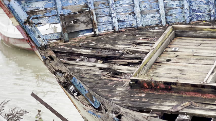 Close-up view of an old abandoned wooden fishing boat wreck with peeling blue and red paint, weathered planks and decaying structure lying on the shore of the Baie de Somme in Le Crotoy, France