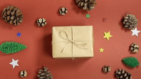 holiday scene featuring hand hold a small brown paper-wrapped gift tied with twine, surrounded by pinecones, glitter stars, and tiny Christmas trees - Powered by Shutterstock - Get 15% off with code: PIKWIZARD15
