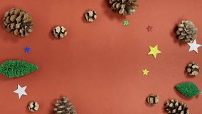holiday scene featuring hand hold a small brown paper-wrapped gift tied with twine, surrounded by pinecones, glitter stars, and tiny Christmas trees - Powered by Shutterstock - Get 15% off with code: PIKWIZARD15