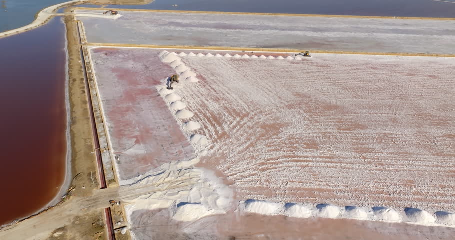 Aerial view of salt mounds in the Trapani salt pans, Sicily, Italy. The waters of the salt evaporation ponds have a characteristic red color. In foreground there are piles of salt. 