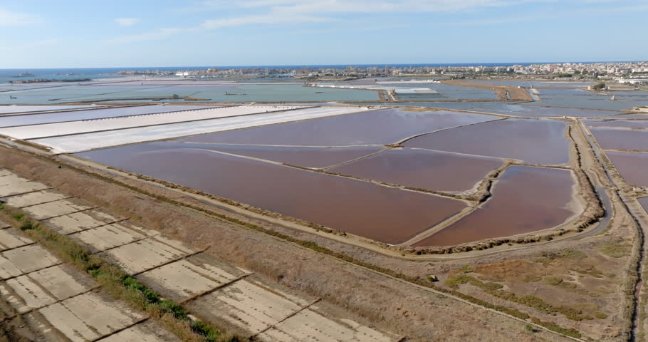 Aerial view of the salt pans and salt extraction plants. In the background, on the horizon, there are Mount Erice and the city of Trapani, Sicily, Italy.