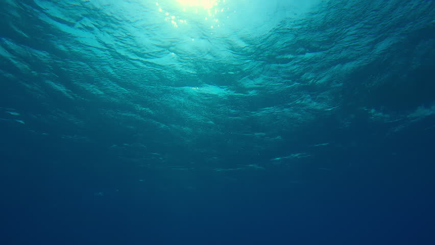 Bottom view on underwater sunlight shine under deep water with ripples on waves surface, View on sunlight from blue abyss, Slow motion of storm waves with sunbeams in the blue depth of Ocean