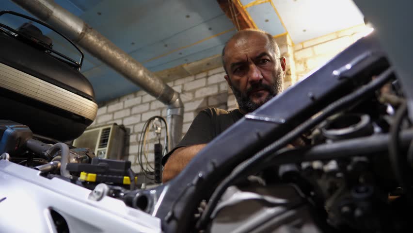 Professional mechanic repairing detail of motorcycle at workplace. Male repairer fixing engine of moto at workshop. Adult repairman mending vehicle motor at garage. Concept of maintenance service - Powered by Shutterstock - Get 15% off with code: PIKWIZARD15