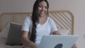 Happy asian woman laughing and talking during a video call on her laptop from the comfort of her bed - Powered by Shutterstock - Get 15% off with code: PIKWIZARD15