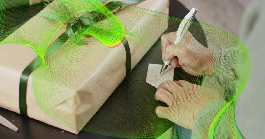 Senior woman hands using pen writing tag, tying dark green ribbon around beige box during crafting. Gift wrapping, crafting, elegance, home decor, celebration, tradition, fine detail