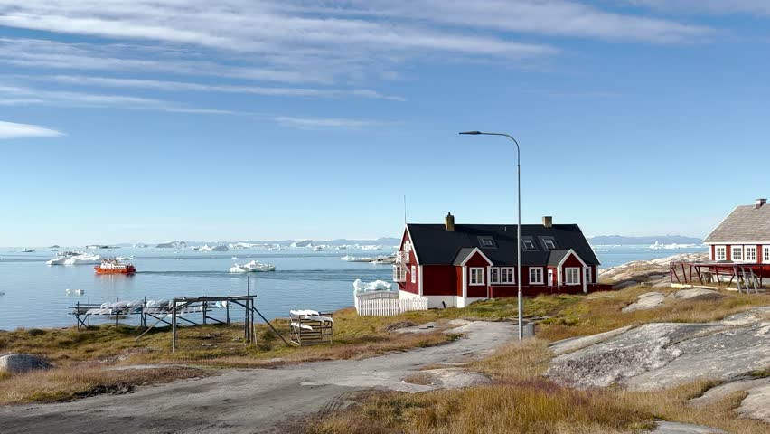 Colorful houses in a small Greenlandic village by the sea with icebergs in the distance