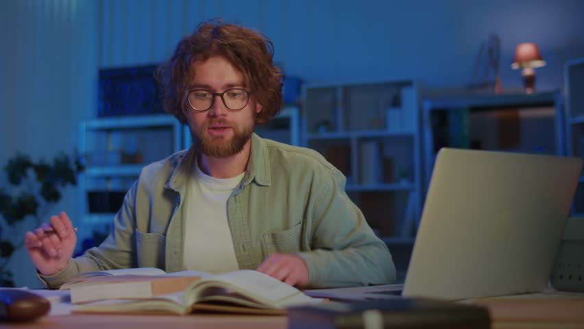 Young Man Reads Book with Deep Focus in Evening Study Environment. Concept of Education, Research, Exam Preparation, and Academic Dedication with Serious Concentration on Knowledge.