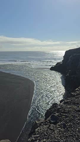 View from Dyrhólaey in Iceland overlooking Reynisfjara beach with Arnardrangur rock and the famous Reynisdrangar cliffs. The sweeping coastline and black sand create a breathtaking coastal panorama.