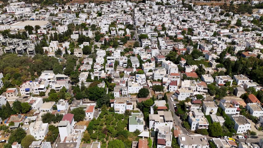 Aerial view of white Mediterranean houses surrounded by green trees on a sunny day in Bodrum, Turkey.