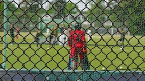 A Chain-link Fence Dominates The Foreground Sharply Contrasting With The Blurred Action Of Field Hockey Players On A Green Sports Field - Powered by Shutterstock - Get 15% off with code: PIKWIZARD15