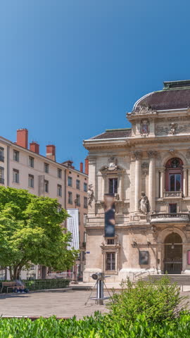 Timelapse hyperlapse of Theatre des Celestins in Lyon, France. A historic theatre on Place des Celestins with trees, benches and people relaxing under blue sky. Classic architecture and cultural charm
