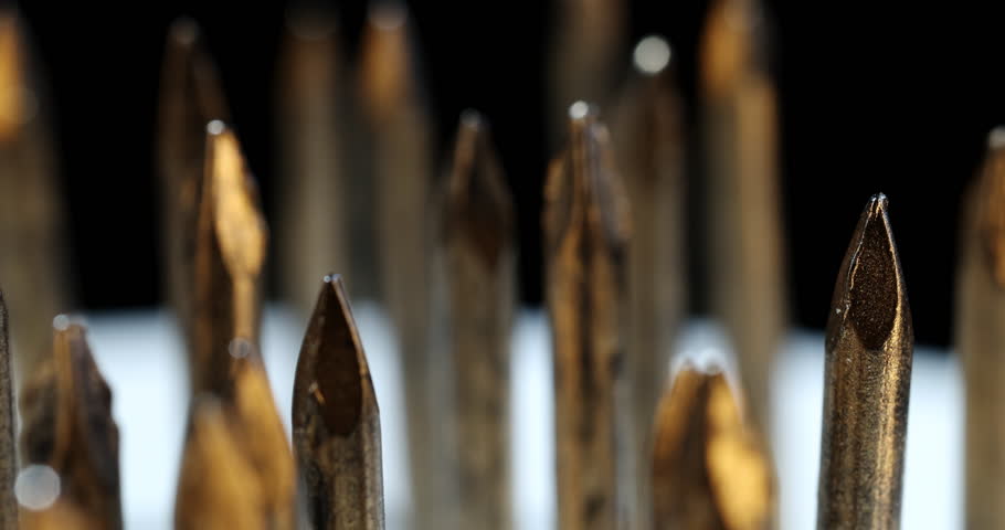 Macro shot of brass drill bits against a bright white background, rotating slowly to reveal detailed metallic surfaces and warm reflections.
