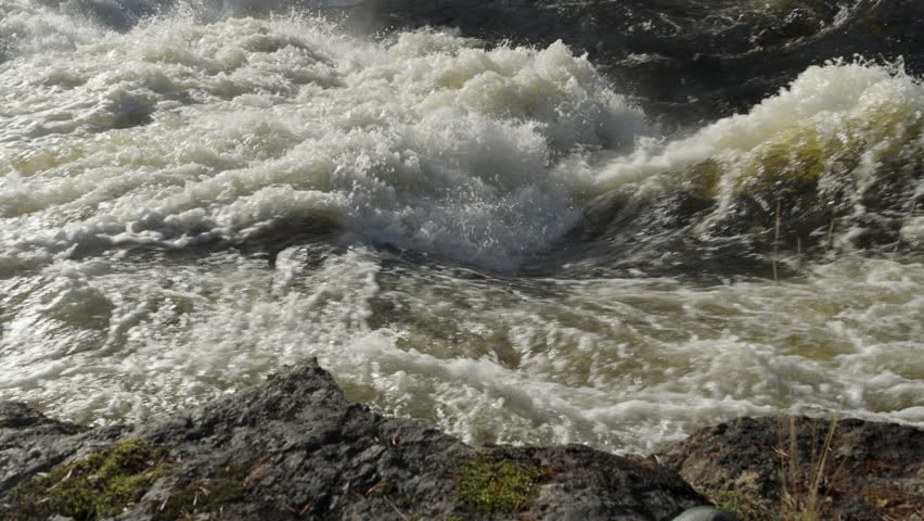 Powerful stream of the Vindel river in Swedish Lapland flowing over rocks on a sunny day. Turbulent white water creating a mesmerizing and powerful display of nature