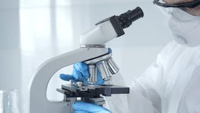 Medical virologist in a hazmat suit, mask, and gloves, diligently working at a microscope in a laboratory researching viruses. Healthcare and science concept - Powered by Shutterstock - Get 15% off with code: PIKWIZARD15