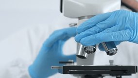 Close up of medical virologist in a hazmat suit, mask, and blue gloves, carefully working at a microscope in a laboratory researching viruses. Medicine and science concept - Powered by Shutterstock - Get 15% off with code: PIKWIZARD15