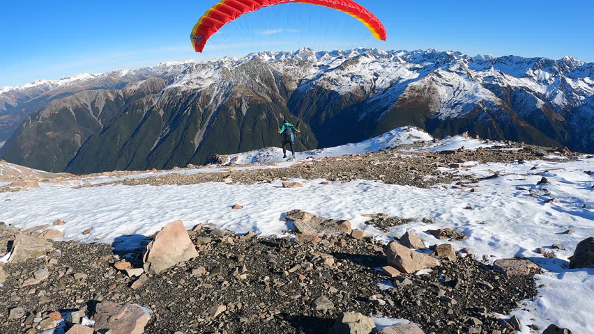 Woman runs and launches into the air with an extreme paraglider on a sunny alpine mountain, showing courage, focus and pure freedom in nature.