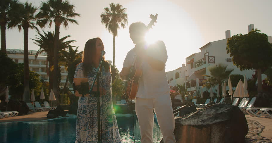 Man and woman perform music by poolside with backlight from evening sun