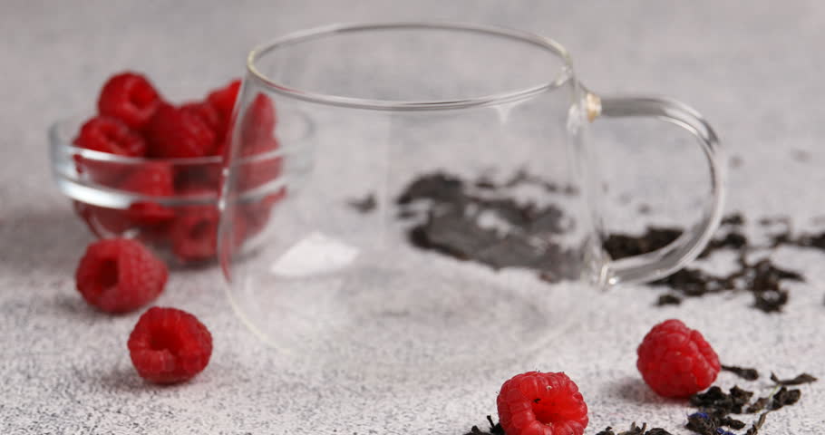 Pouring tea into cup, raspberries and brew on light table, closeup