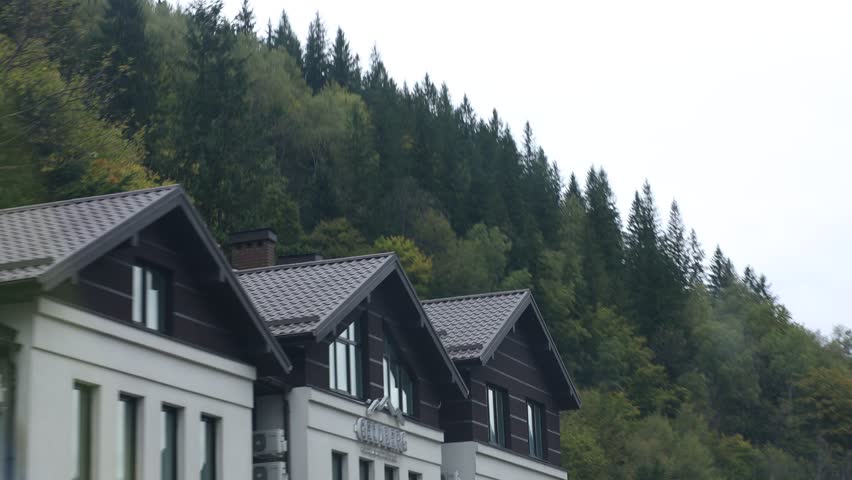 Buildings and green trees in mountains, view from moving car