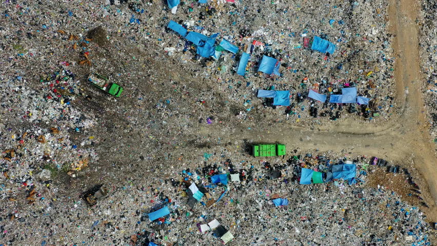 Aerial timelapse of a busy landfill operations: a green garbage truck dumps trash, scavengers sort recyclables, and a bulldozer levels the refuse.