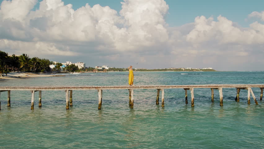 Person in summer dress standing on a pier looking out at ocean with birds flying in Mexico