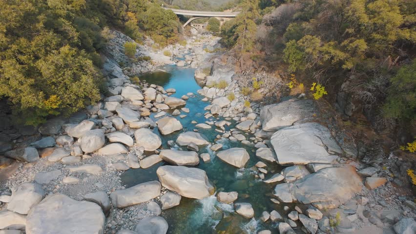 FPV drone flying under a rustic bridge across the South Yuba River in California. Golden trees and granite rocks line the forested canyon in this scenic 4K autumn adventure shot.