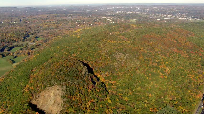 Aerial view of autumn foliage covering rolling hills and distant cityscape horizon