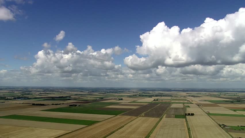 Aerial view of patchwork farmland under a blue sky filled with fluffy clouds