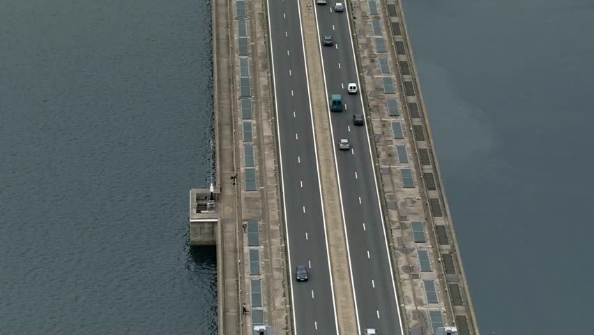 Aerial view of a long concrete bridge with traffic over dark blue water surface