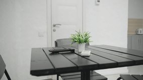 Modern dining table with black wooden surface featuring a small potted plant, remote control, and smartphone. A white door in the background leads to a well lit space with minimalistic design - Powered by Shutterstock - Get 15% off with code: PIKWIZARD15