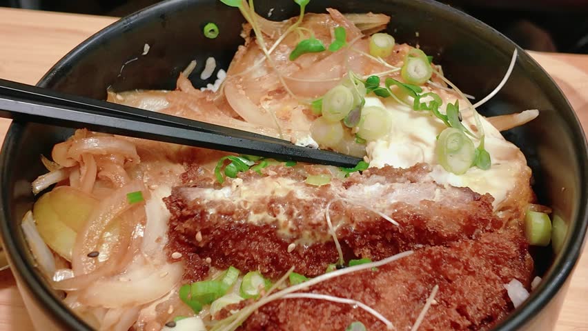 Delicious katsudon served in a bowl, showcasing crispy pork cutlet, eggs, and onions over rice, garnished with fresh green onions