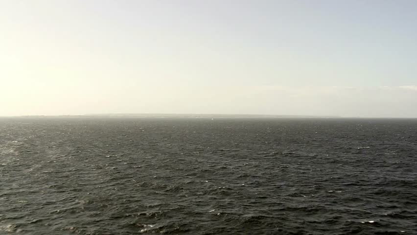Dark ocean water with distant land under a pale sky creating a somber seascape