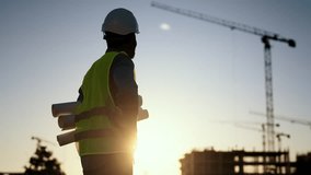 Auditor or architect expert examining construction, male silhouette in sunset. Professional builder or foreman standing on building site, tall construction cranes against blue sky and bright sun - Powered by Shutterstock - Get 15% off with code: PIKWIZARD15