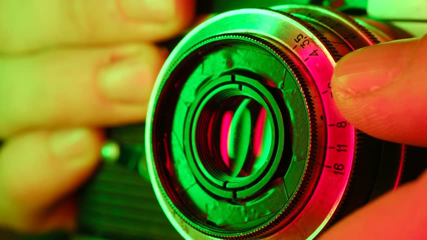 Close up view of a photographer hand manually adjusting the aperture ring on an old fashioned camera lens, with vibrant green and red light creating a stylish, retro atmosphere