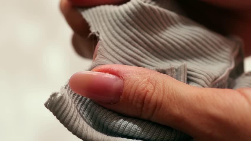 Female hands tearing fabric in half, close-up.