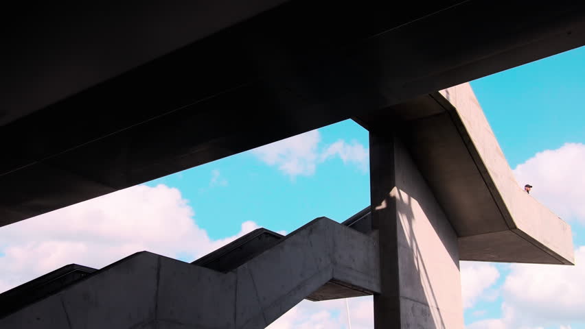 Man walks down concrete stairway on bridge surrounded by blue sky in Gothenburg, Sweden