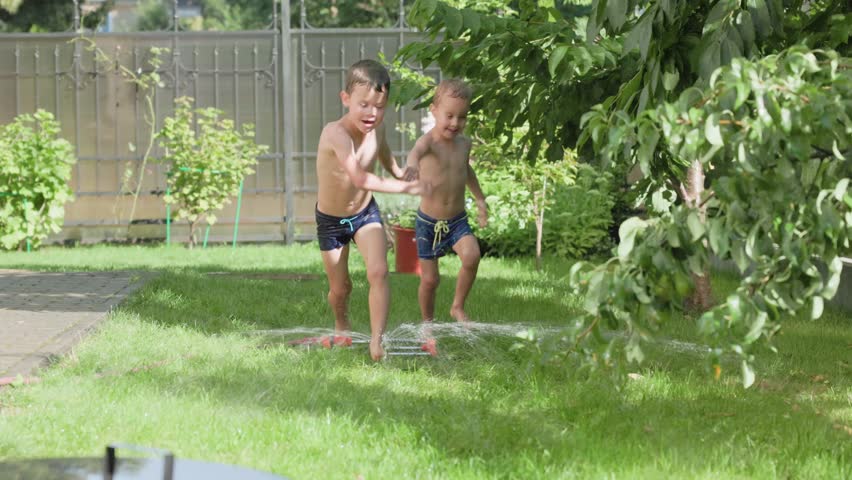 Excited kids joyfully run through a vibrant garden sprinkler on a sunny day, relishing all the summer fun