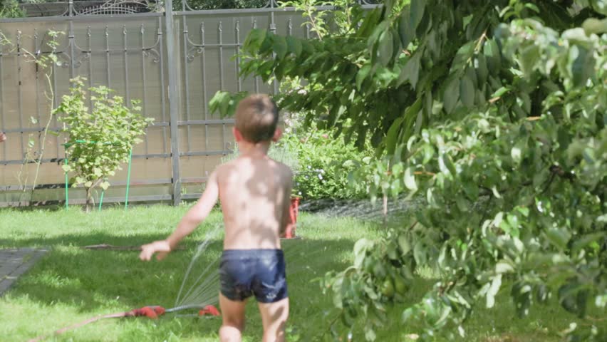 Two joyful kids are playing happily in a garden under the sun, enjoying refreshing water from a sprinkler