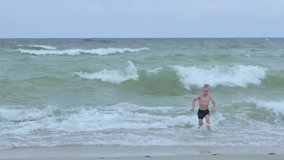 Boy 4 years blue swim trunks alone beach storm waves high tide child near sea no supervision danger risky environment unsupervised minor coast full body visible wet sand emergency awareness parenting - Powered by Shutterstock - Get 15% off with code: PIKWIZARD15