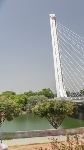 Alamillo Bridge with a tall pylon and steel cables spans over the Guadalquivir River in Seville, Spain. Timelapse hyperlapse of modern suspension design with busy traffic under a clear blue sky.