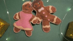 Fake gingerbread couple cookies decorated with icing on green background among gifts and lights, creating cheerful Christmas atmosphere. Felt ornaments are hand-sewn and embellished. Love couple - Powered by Shutterstock - Get 15% off with code: PIKWIZARD15