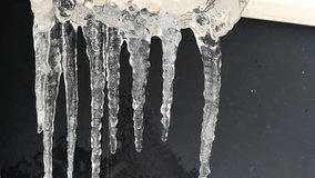 Icicles are melting. Several long, elongated, translucent white icicles hang nearby. Water trickles down them, and droplets fall as they break off. The ice melts, snowflakes fly past. - Powered by Shutterstock - Get 15% off with code: PIKWIZARD15