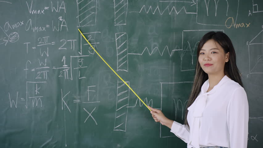 Back to school in summer. Happy Asian young female math teacher standing holding a pointer and teaching a mathematics lesson on blackboard in front of the classroom, Concept of learning and education. - Powered by Shutterstock - Get 15% off with code: PIKWIZARD15