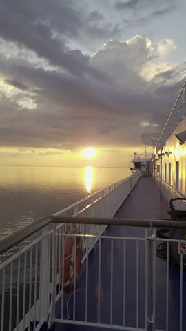 Beautiful golden sunset reflecting on the calm waters of the Baltic Sea, viewed from the moving deck of a passenger ferry with dramatic clouds filling the sky during a peaceful evening voyage