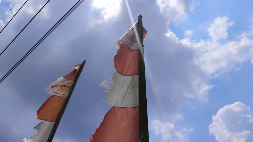 The scene of bright prayer flags fluttering along vertical poles under a clear blue sky, the sunlight gently shining down. 