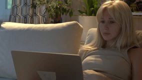 A young woman with blond hair sits on the sofa and looks at the laptop. - Powered by Shutterstock - Get 15% off with code: PIKWIZARD15